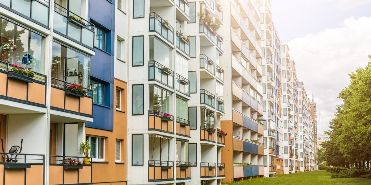 Modern apartment complex with multiple balconies and large windows, surrounded by greenery.